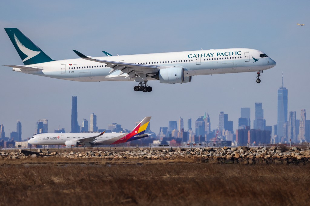 A Cathay Pacific Airbus A350 from Hong Kong prepares to land at JFK International Airport with the Manhattan skyline in the background